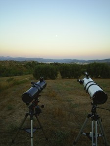 Two telescopes in a field pointing at the clear evening sky.